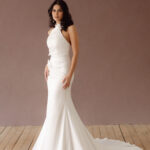 Fabric is Satin, silhouette is Fit and Flare / Modified A-Line, neckline is Halter, sleeve style is Sleeveless, train is Chapel Train, waistline is Natural Ruched, embellishment is 3D Floral Appliqué, back is Low V-Back, color is Ivory, style is Modern Minimalist Romance, Smooth satin with 3D floral details and a removable train for two distinct bridal looks.