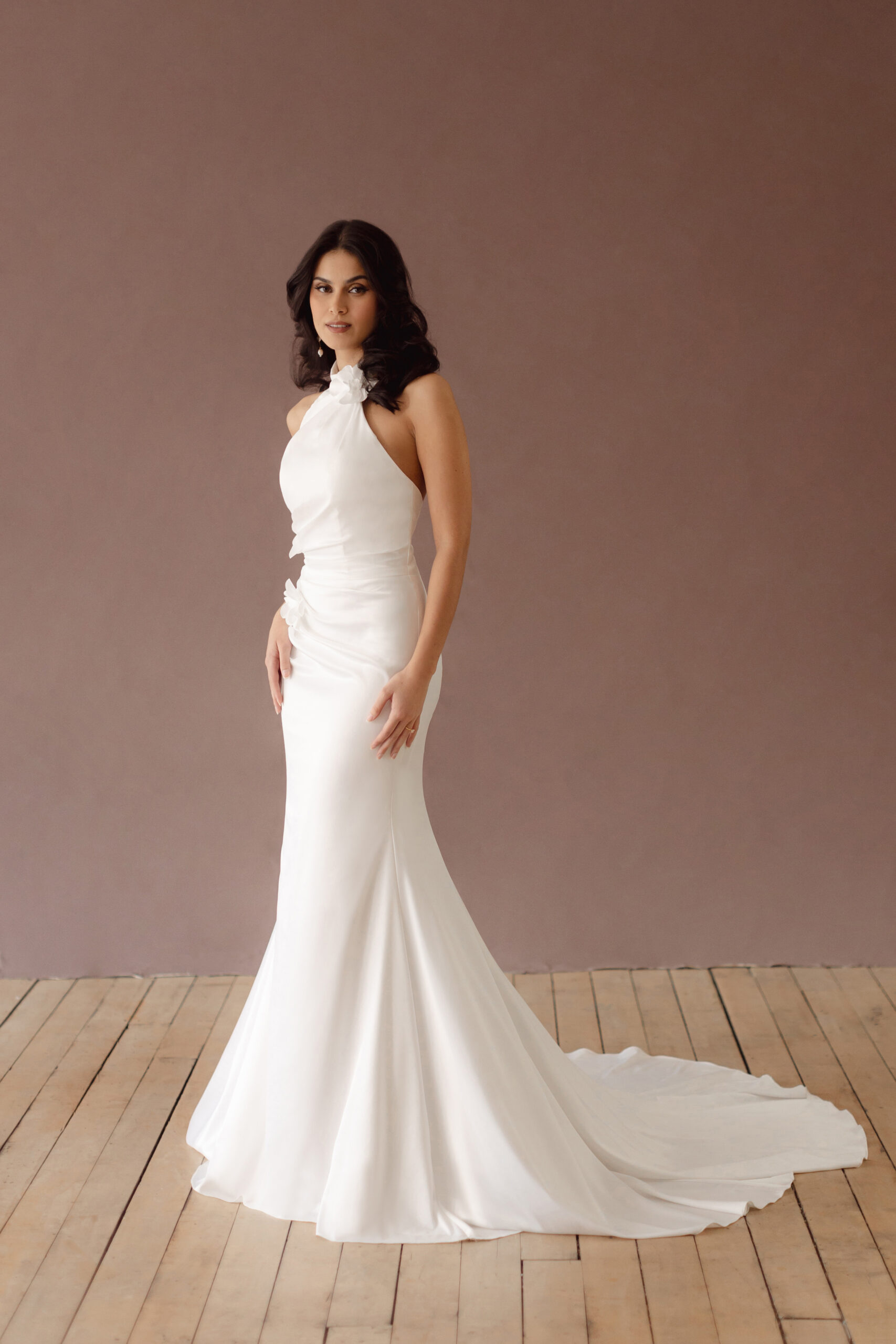 Fabric is Satin, silhouette is Fit and Flare / Modified A-Line, neckline is Halter, sleeve style is Sleeveless, train is Chapel Train, waistline is Natural Ruched, embellishment is 3D Floral Appliqué, back is Low V-Back, color is Ivory, style is Modern Minimalist Romance, Smooth satin with 3D floral details and a removable train for two distinct bridal looks.