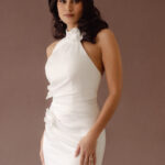 Fabric is Satin, silhouette is Fit and Flare / Modified A-Line, neckline is Halter, sleeve style is Sleeveless, train is Chapel Train, waistline is Natural Ruched, embellishment is 3D Floral Appliqué, back is Low V-Back, color is Ivory, style is Modern Minimalist Romance, Smooth satin with 3D floral details and a removable train for two distinct bridal looks.