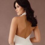 Fabric is Satin, silhouette is Fit and Flare / Modified A-Line, neckline is Halter, sleeve style is Sleeveless, train is Chapel Train, waistline is Natural Ruched, embellishment is 3D Floral Appliqué, back is Low V-Back, color is Ivory, style is Modern Minimalist Romance, Smooth satin with 3D floral details and a removable train for two distinct bridal looks.