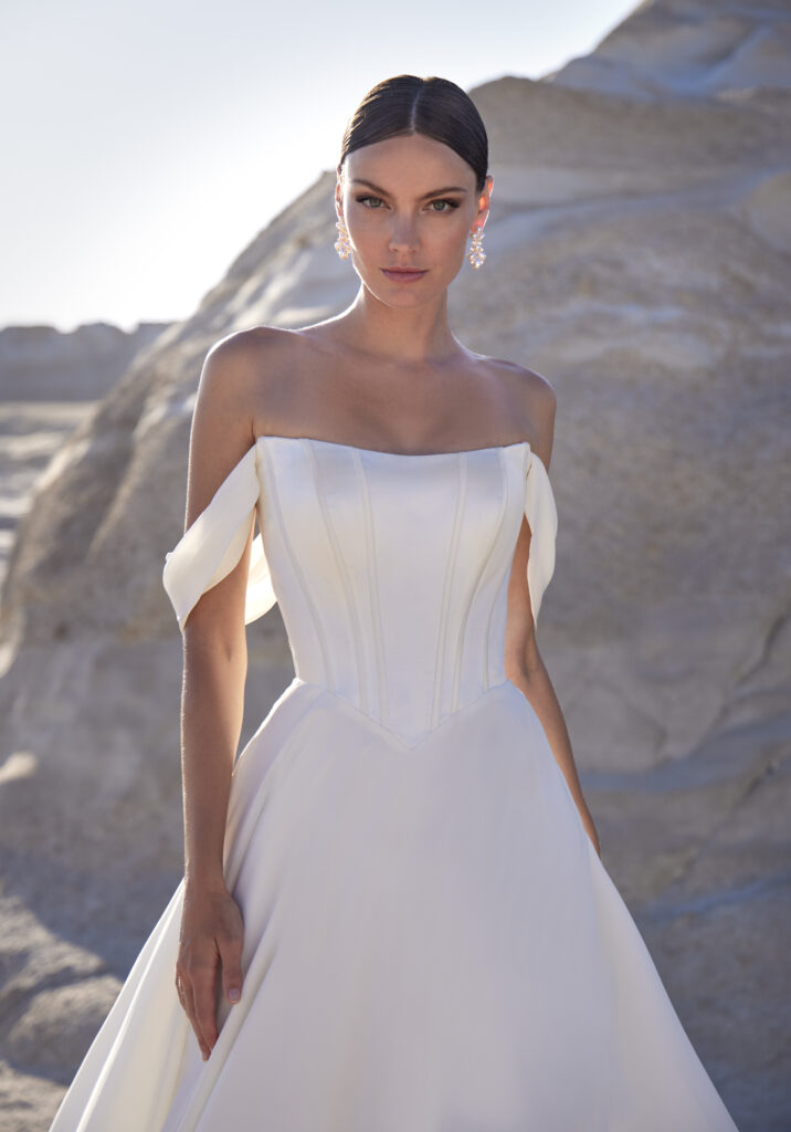 Fabric is Satin & Chiffon, silhouette is A-line, neckline is Cat eye neckline, sleeve style is Off-the-shoulder, train is Chapel, waistline is Basque, embellishment is Covered buttons, back is Button-up back, color is Ivory, style is Minimalist Romance, Boned bodice, soft drape