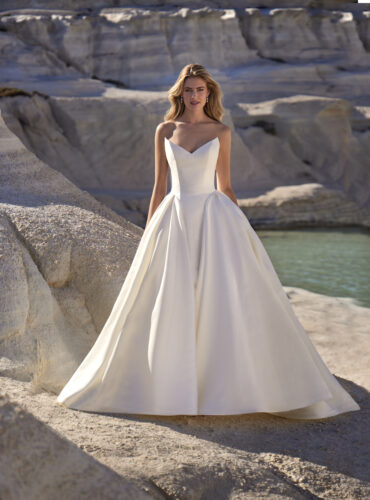 Fabric is Mikado, silhouette is Ballgown, neckline is Cat eye neckline, sleeve style is Strapless, train is Cathedral, waistline is Basque, embellishment is Fabric folds / Structure, back is Button-down, color is Ivory, style is Modern Classic, Sculptural lines, voluminous skirt, clean finish