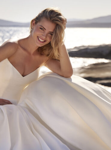 Fabric is Mikado, silhouette is Ballgown, neckline is Cat eye neckline, sleeve style is Strapless, train is Cathedral, waistline is Basque, embellishment is Fabric folds / Structure, back is Button-down, color is Ivory, style is Modern Classic, Sculptural lines, voluminous skirt, clean finish