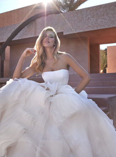 Fabric is Organza, silhouette is Ball Gown, neckline is Strapless Straight, sleeve style is Sleeveless, train is Cathedral, waistline is Natural, embellishment is Ruffled Layers, back is Straight Back, color is Ivory, style is Modern Minimalist, Structured Bodice, Layered Skirt