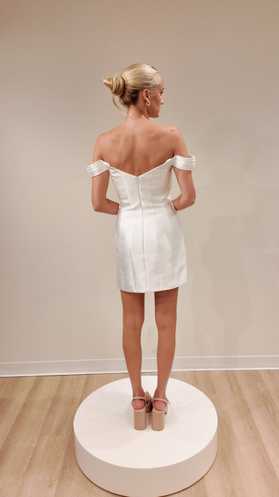 Fabric is Satin, silhouette is Sheath Mini, neckline is Sweetheart, sleeve style is Off-Shoulder, train is No Train, waistline is Natural, embellishment is Minimalist, back is Zip Back, color is Ivory, style is Modern Minimalist, Structured seams, short bridal dress, clean lines